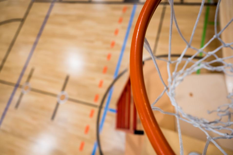 Nahaufnahme eines Basketballkorbs mit Netz über einem aufgezeichneten Basketballfeld aus Holz.