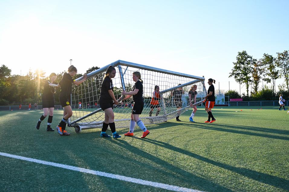 Mannschaft von Fußballspielerinnen hebt ein Tor auf einem Kunstrasenplatz bei Sonnenuntergang an.