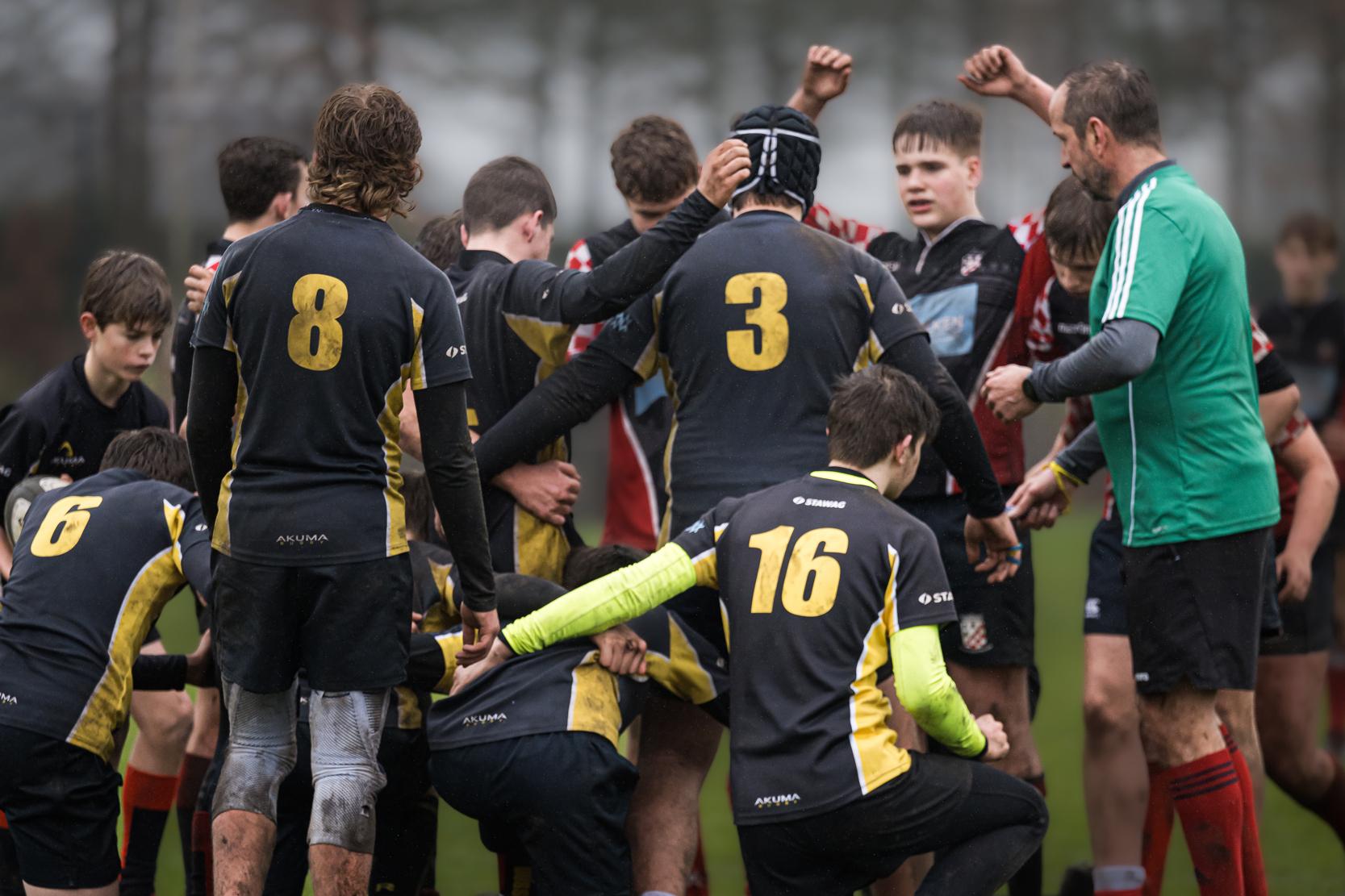 Gruppenspieler auf einem Rugbyfeld umarmen sich, einige tragen die Trikots mit den Nummern 3, 8 und 16.