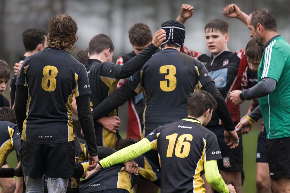 Gruppenspieler auf einem Rugbyfeld umarmen sich, einige tragen die Trikots mit den Nummern 3, 8 und 16.