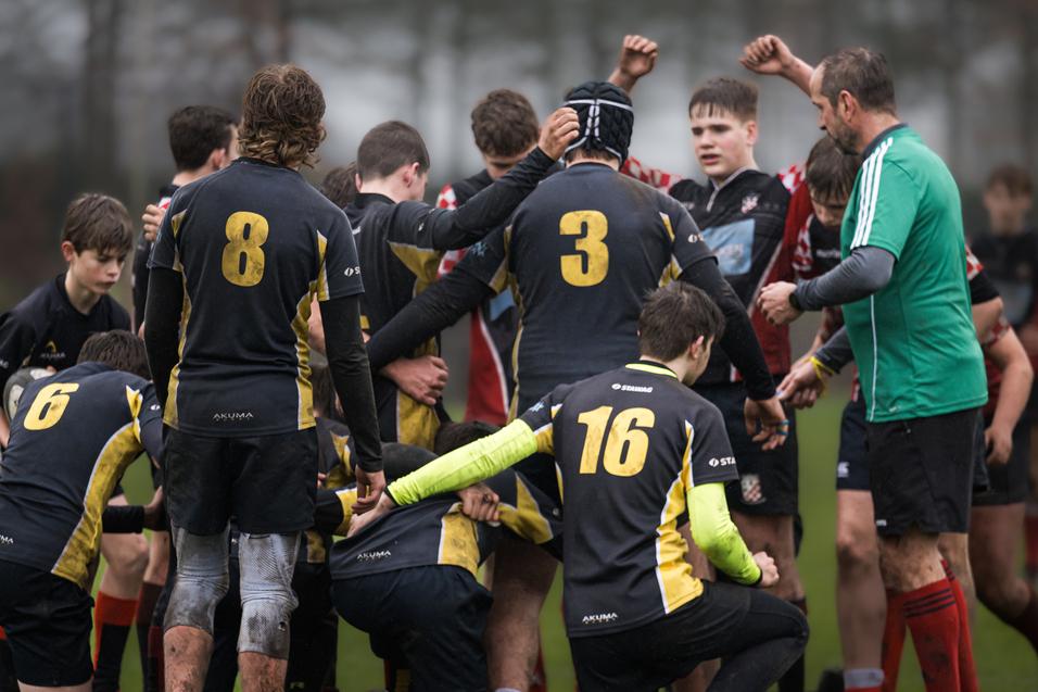 Gruppenspieler auf einem Rugbyfeld umarmen sich, einige tragen die Trikots mit den Nummern 3, 8 und 16.
